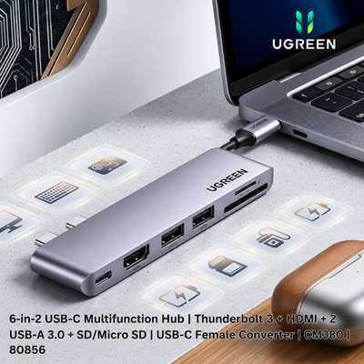 UGREEN 6-in-2 USB-C multifunction hub shown connected to a laptop on a light gray desk surface. The hub is silver aluminum with multiple ports and visible UGREEN branding.