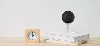IMOU Cue 2 indoor camera on a shelf next to a clock and books, lifestyle
